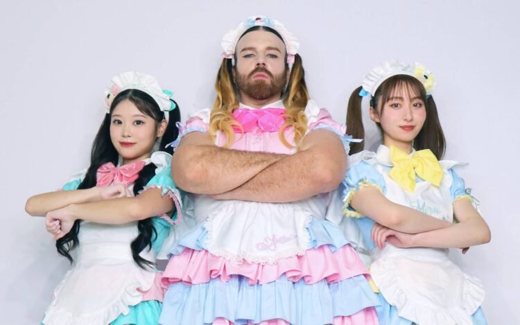 The three members of BABYBEARD, dressed in colourful dresses, in light/pastel pink, blue and green, with puffy short sleeves and bows, are standing next to each other while having their arms crossed. LADYBEARD (in pink) stands in the centre of the photo, Suzu (green) on the left and Mizuki (blue) on the right.