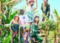 The photograph shows six members of Super Jet Kinoko striking various poses on a staircase, surrounded by green plants. All members are wearing colourful clothing, some complemented by colourful headwear and sunglasses.