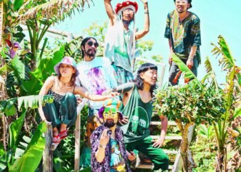 The photograph shows six members of Super Jet Kinoko striking various poses on a staircase, surrounded by green plants. All members are wearing colourful clothing, some complemented by colourful headwear and sunglasses.
