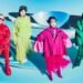 The four members of ExWHYZ in colourful outfits standing in a blue room with a futuristic looking background. Each member is dressed in a vibrant attire, all in a different colour.
