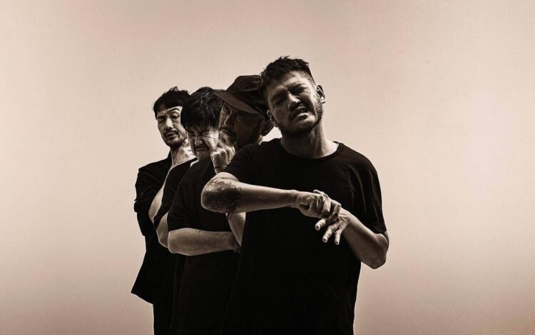 A monochromatic photo of the four members of the Japanese instrumental rock band toe, posing behind each other with various (dramatic) facial expressions, with the eyes closed. All are dressed in dark/black clothing.