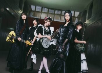 Photo shows the five members of BAND-MAID, from left to right: Misa, Akane, Miku, Saiki, and Kanami, partly dressed in maid-inspired clothing and partly dressed in black attire. Apart from the vocalist, they are all holding their instruments. © BAND-MAID
