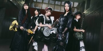 Photo shows the five members of BAND-MAID, from left to right: Misa, Akane, Miku, Saiki, and Kanami, partly dressed in maid-inspired clothing and partly dressed in black attire. Apart from the vocalist, they are all holding their instruments. © BAND-MAID