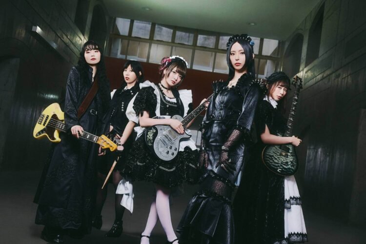Photo shows the five members of BAND-MAID, from left to right: Misa, Akane, Miku, Saiki, and Kanami, partly dressed in maid-inspired clothing and partly dressed in black attire. Apart from the vocalist, they are all holding their instruments. © BAND-MAID