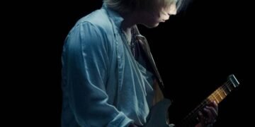 Photo captures Ichika Nito holding and playing his electric guitar in a dimly lit location, with a black background. It seems to be part of a photo shoot for his first album. © Ichika Nito