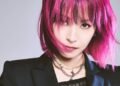 A cropped version of a vertical photo of LiSA with pink hair in a bob-style and a black jacket with a leather corset. Photo by Hirohisa Nakano