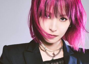 A cropped version of a vertical photo of LiSA with pink hair in a bob-style and a black jacket with a leather corset. Photo by Hirohisa Nakano