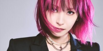 A cropped version of a vertical photo of LiSA with pink hair in a bob-style and a black jacket with a leather corset. Photo by Hirohisa Nakano