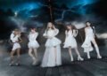 The photo features the five women of LOVEBITES posing together while standing on a ship and dark clouds with lightning on the background. They are uniformly dressed in white/off-white with gold elements outfits, each incorporating their personal style.