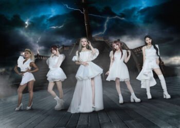 The photo features the five women of LOVEBITES posing together while standing on a ship and dark clouds with lightning on the background. They are uniformly dressed in white/off-white with gold elements outfits, each incorporating their personal style.