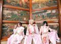 Seth, Kouki and Tsukasa of Sakura Zensen dressed in traditional kimono with hakama, with pink and red hues and floral patterns. They are seated side by side with Japanese (wooden) artworks in the background. © Sakura Zensen