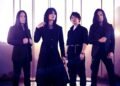 Photo of the four-piece alternative metal band Esprit D'Air standing side by side on a location with a mountain range on the background. All the members are dressed in black clothing, with gothic and metal elements.
