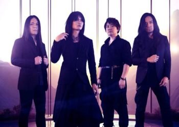 Photo of the four-piece alternative metal band Esprit D'Air standing side by side on a location with a mountain range on the background. All the members are dressed in black clothing, with gothic and metal elements.