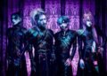 The photo features the four members of JILUKA, dressed in distinct dark, gothic attire with silver face jewelry (such as a chin, eye or ear piece) posing against a purple gothic-themed screen.