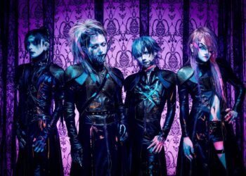 The photo features the four members of JILUKA, dressed in distinct dark, gothic attire with silver face jewelry (such as a chin, eye or ear piece) posing against a purple gothic-themed screen.