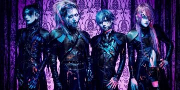 The photo features the four members of JILUKA, dressed in distinct dark, gothic attire with silver face jewelry (such as a chin, eye or ear piece) posing against a purple gothic-themed screen.