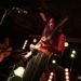 Bandleader of Hibushibire, Changchang, plays the guitar on the stage of The Victoria in Birmingham. The musician is wearing colourful clothing, a reddish shirt and vertical striped pants in the colours green, red, and yellow. In the background there is another member, Tetsuji Toyoda, playing the bass. Photography JJ Grant (wonderlens)