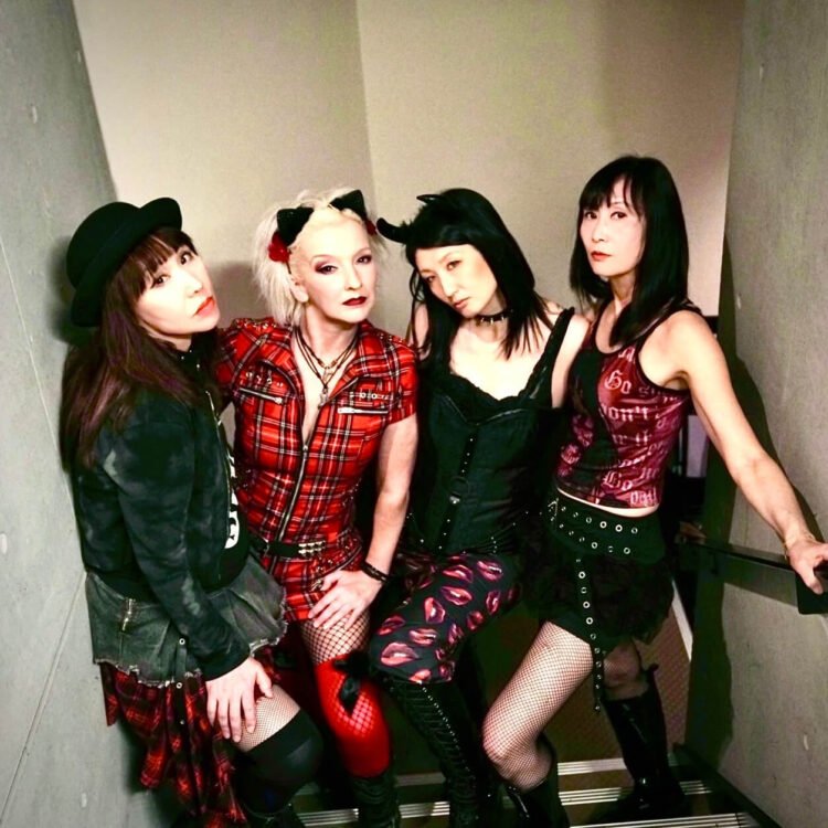 The photo features the four members of MIKABOMB (Also written as MIKA BOMB), all dressed in an alternative fashion style, wearing punk-inspired attire. They are standing close together on a flight of stairs.