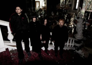 The four members of kokeshi standing on a staircase of an old building that is filled with statues, while it seems to be derelict and maybe also declared unfit for habitation. All members are dressed in black clothing and not looking into the camera lens. © kokeshi