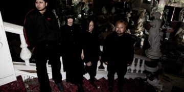 The four members of kokeshi standing on a staircase of an old building that is filled with statues, while it seems to be derelict and maybe also declared unfit for habitation. All members are dressed in black clothing and not looking into the camera lens. © kokeshi