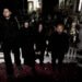 The four members of kokeshi standing on a staircase of an old building that is filled with statues, while it seems to be derelict and maybe also declared unfit for habitation. All members are dressed in black clothing and not looking into the camera lens. © kokeshi