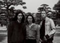 Black-and-white photo of the three members of Tō Yō facing the camera. They are standing together in a park with the background filled with trees. Photo by Takaumi Minagawa