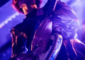 Focus on Mari of TsuShiMaMiRe on stage of Musicon in The Hague, while she is playing her guitar. De full focus goes onto her hands. The stage lighting is at full power, making the musician glow a bit. Photography: Francisca Hagen (AVO Magazine)