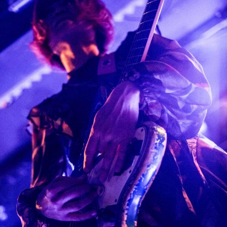 Focus on Mari of TsuShiMaMiRe on stage of Musicon in The Hague, while she is playing her guitar. De full focus goes onto her hands. The stage lighting is at full power, making the musician glow a bit. Photography: Francisca Hagen (AVO Magazine)
